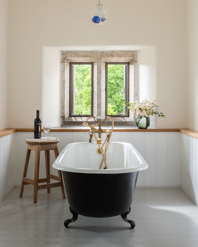 Morwell: a black, clawfoot bathtub in front of a stone window with a milk stool to the left