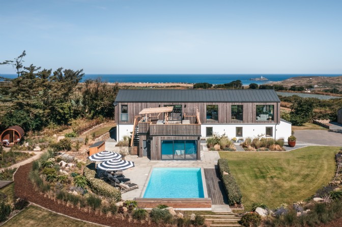 A large, half wood-clad property with a rectangular lawn pool and large windows called Senara in Gwithian, Cornwall