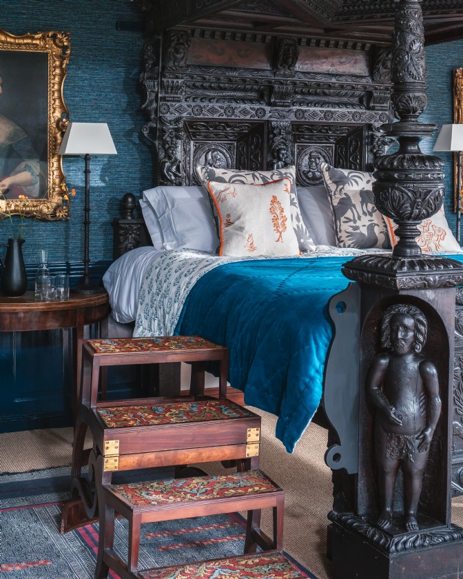 A dramatic, black, carved four-poster bed in a blue room at Gulliver's Hall, one of the storybook homes in Britain