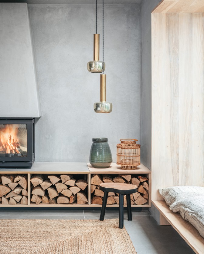 A modern industrial lounge with a woodburner above logs and dangling lights