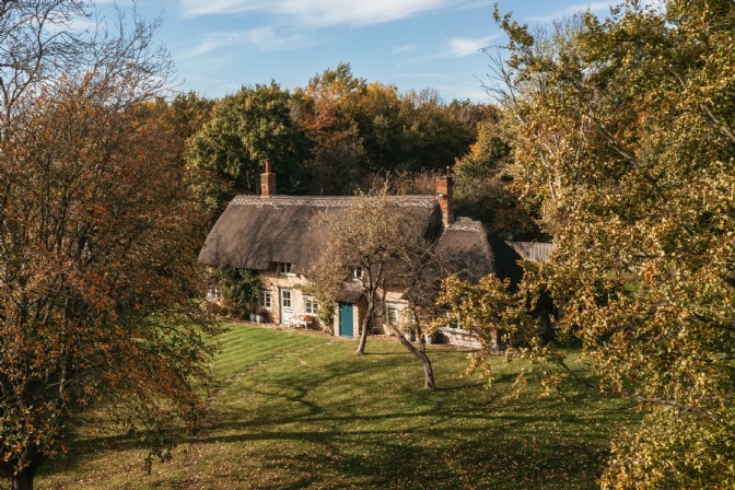 White Crow Cottage: a thatched roof cottage in a large garden surrounded by trees