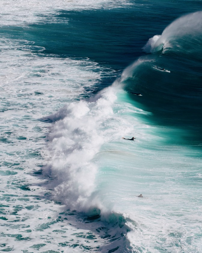 A bird's-eye view of the ocean with frothing waves and surfers