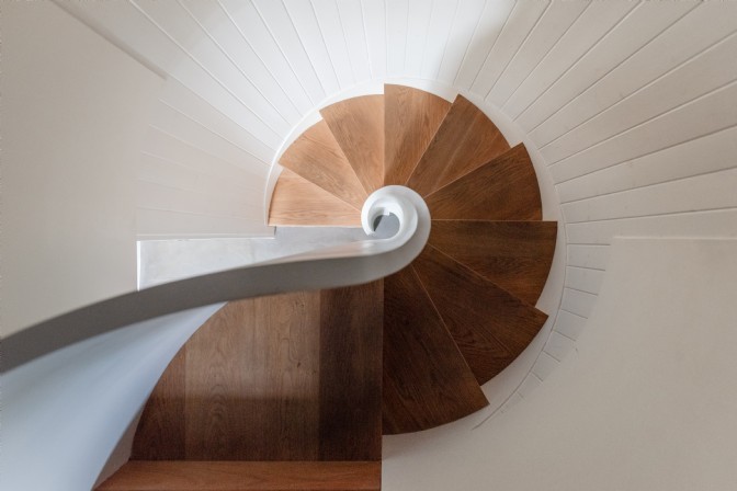 An aeriel shot of an oak spiral staircase with white walls and banister 