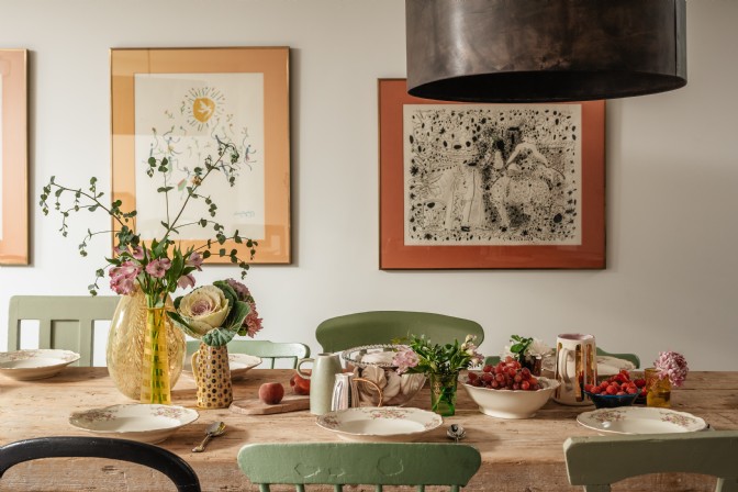 A set dining table covered in flowers and fruit, with Picasso prints on the wall behind