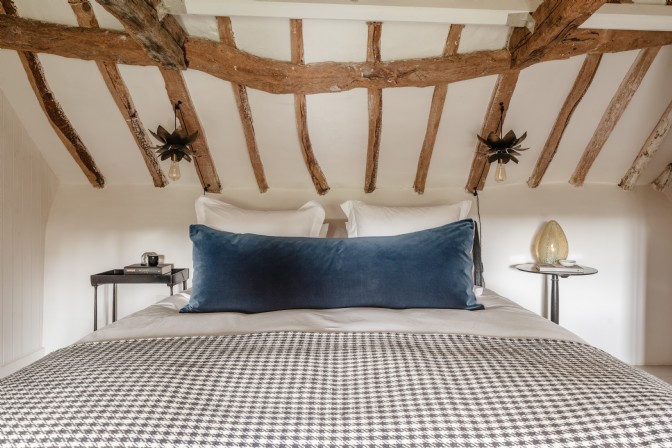 A large bed set under timber beams and chandeliers. The bedding is gingham and there is a large blue cushion