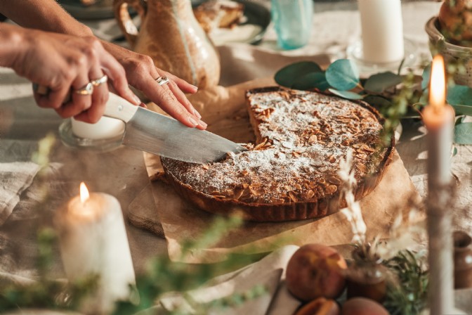 An image of someone cutting a tart from above. The table is covered in foliage, candles and food.