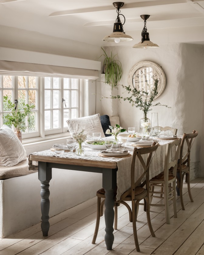 A whitewashed cottage dining room with an oak table in front of a window at The Fable