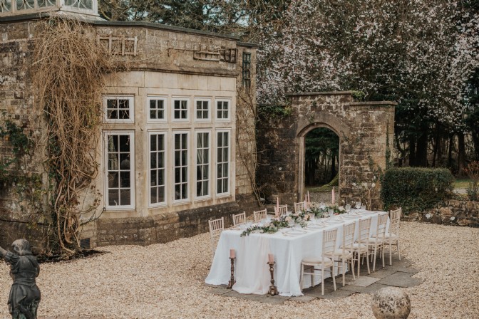 A long table set for fine dining in a pebble courtyard outside of a manor, at Florin