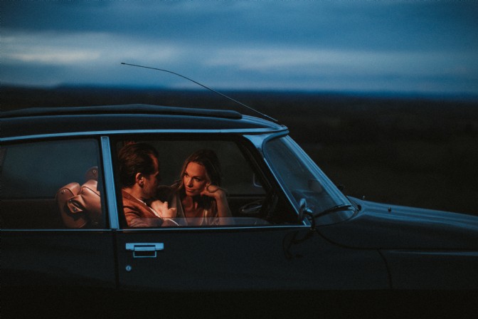 An image of a couple in a black car at dusk. 