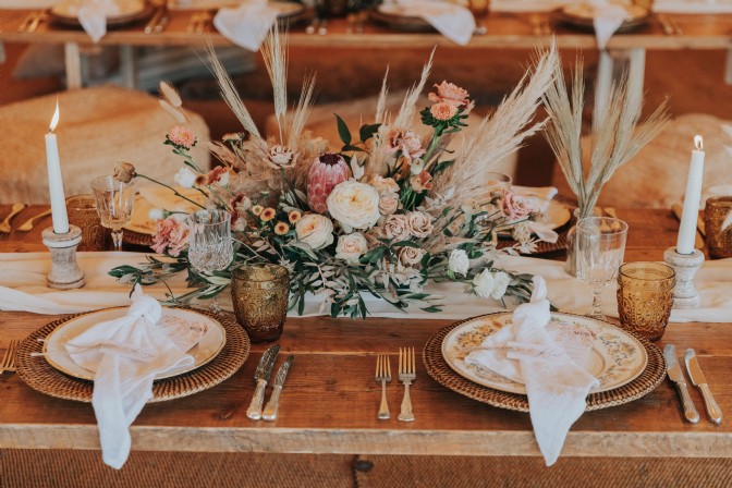 An image of a table set up for a wedding. There are lit candles, napkins on plates and flowers.