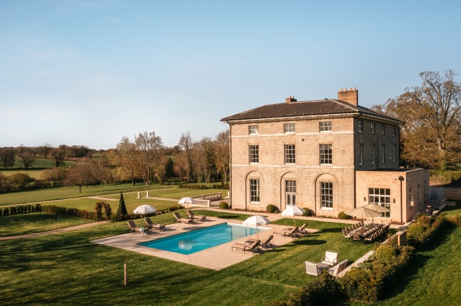 A Georgian manor with a rectangular pool, surrounded by landscaped lawns and autumn trees