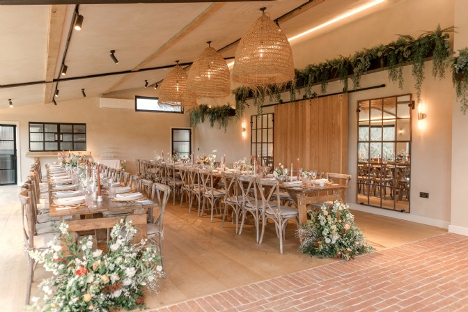 Two long banquet tables in a modern barn with flowers, candles, and place settings