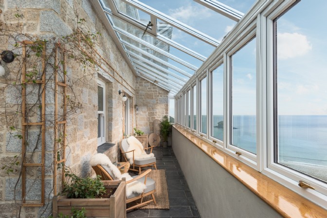 A long conservatory hallway with an exposed stone wall and glass side, overlooking the ocean