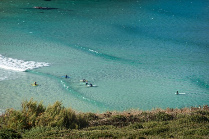 Surfers in wetsuits sit on their boards in Mawgan Porth in Cornwall
