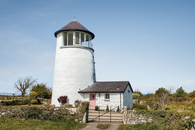 A white lighthouse with a pink door on the coast on the Isle of Anglesey in Wales