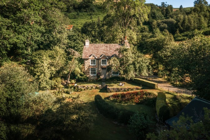 An image of a cottage in the mountains, surrounded by green trees